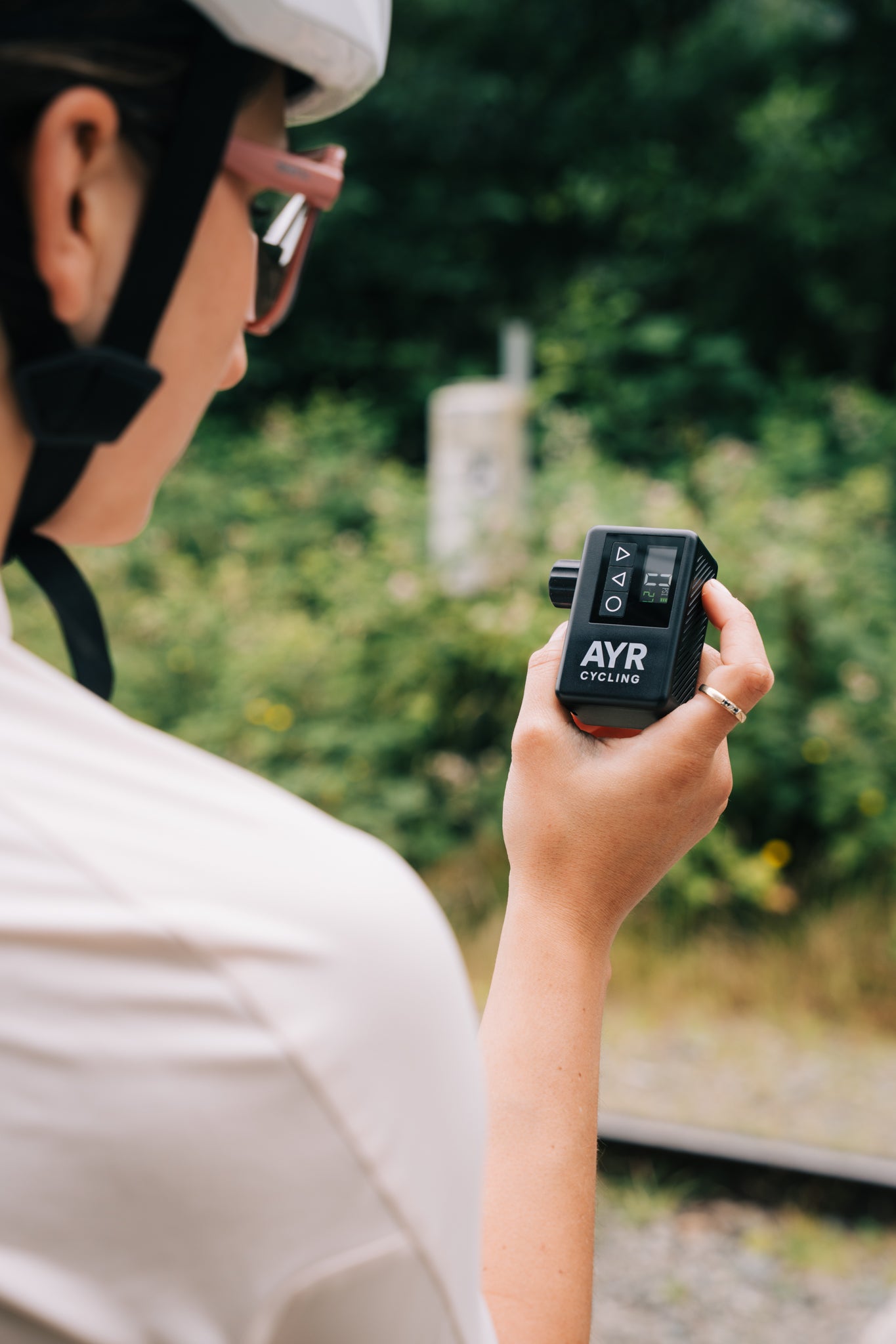 Cyclist holding AYR Cycling electric bike pump in hand while checking PSI on digital display, forest trail background