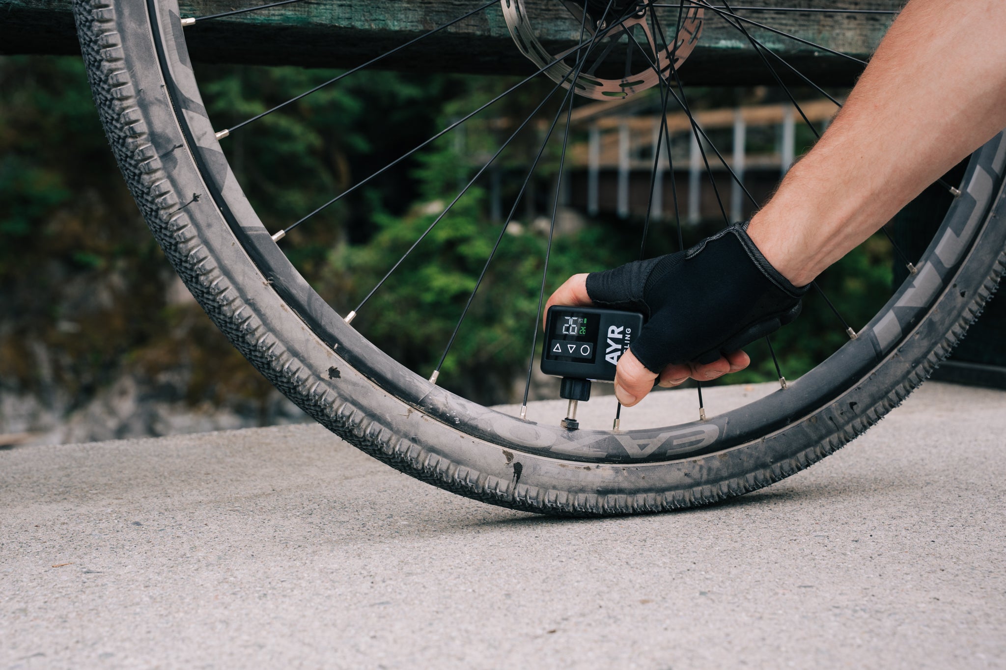 Cyclist using AYR Cycling E-Pump on a gravel bike near a bridge, showing digital PSI display