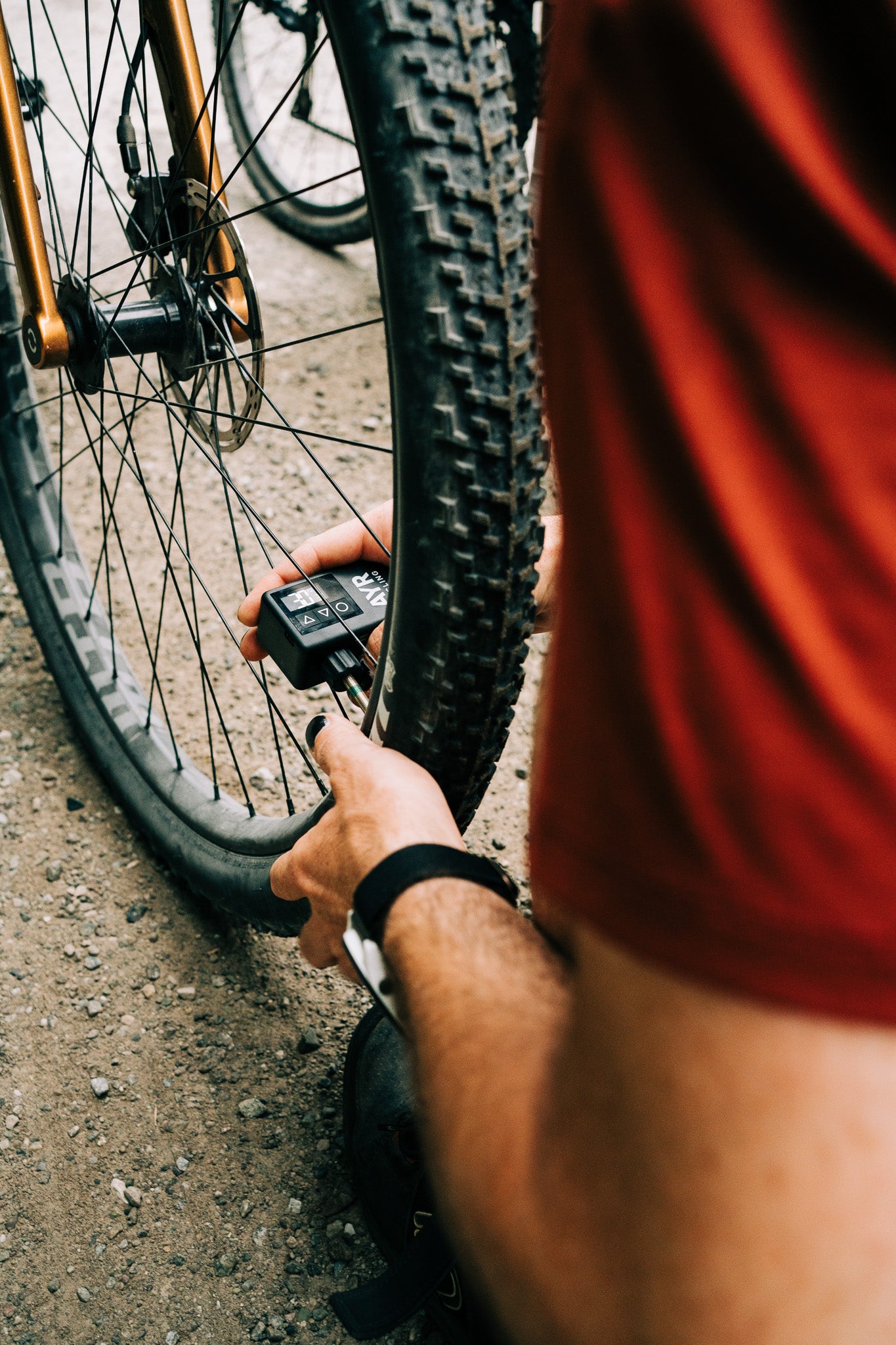 Cyclist using AYR Cycling electric pump to inflate a mountain bike tire on a gravel trail, close-up of hands and device in action