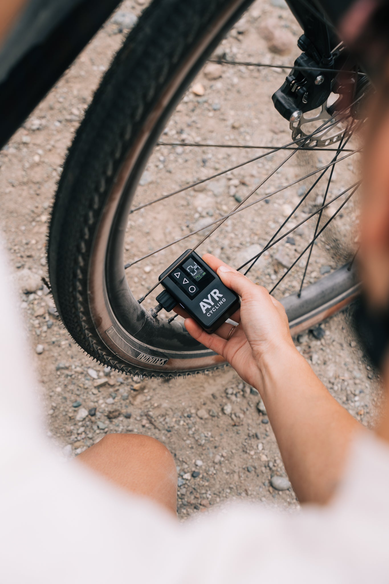 Cyclist using the AYR electric bike pump to inflate a gravel bike tire on a dirt trail.