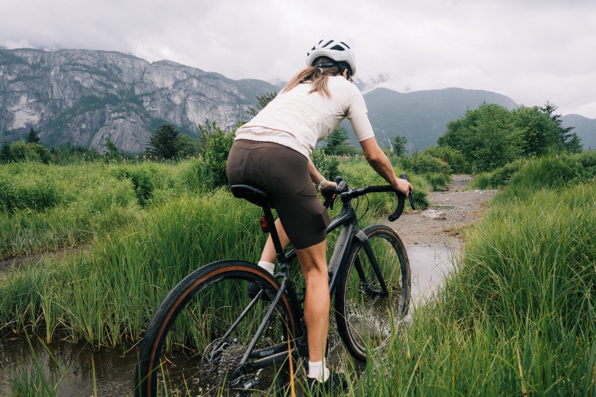 Gravel cyclist riding through a lush trail in Squamish with mountains in the background